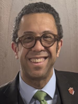 This is a headshot of a man wearing a suit and tie with eye glasses.