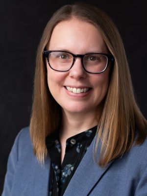 This is a photograph of a woman wearing glasses in professional attire.
